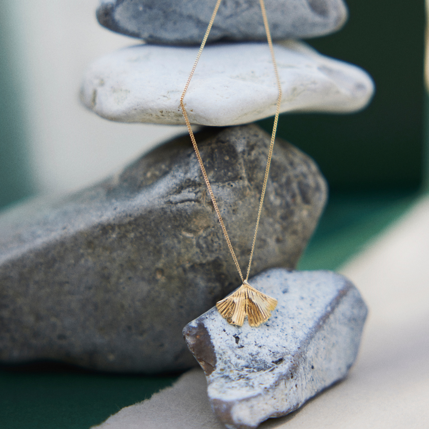 Beautiful exclusive gold necklace with a pendant shaped as a Ginkgo Biloba leaf balancing on an elegant pile of rocks. 18 karat, recycled solid gold.